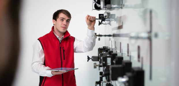 Schulungsteilnehmer vor Hydraulik-Schulungsanlage mit Komponenten Ein Schulungsteilnehmer mit roter Weste steht vor einer Hydraulik-Schulungsanlage mit verschiedenen Hydraulik-Komponenten.
