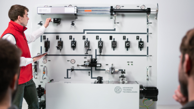 Schulungsteilnehmer vor Hydraulik-Schulungsanlage Ein Schulungsteilnehmer in roter Weste steht vor einer großen Hydraulik-Schulungsanlage.