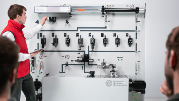 Schulungsteilnehmer vor Hydraulik-Schulungsanlage Ein Schulungsteilnehmer in roter Weste steht vor einer großen Hydraulik-Schulungsanlage.